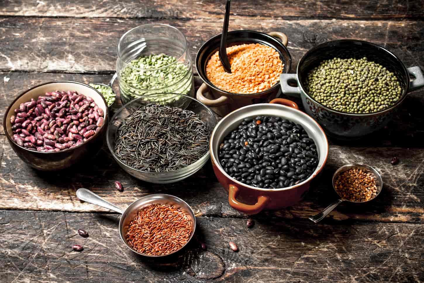 An image of various bean seeds in a bowl on a wooden table.