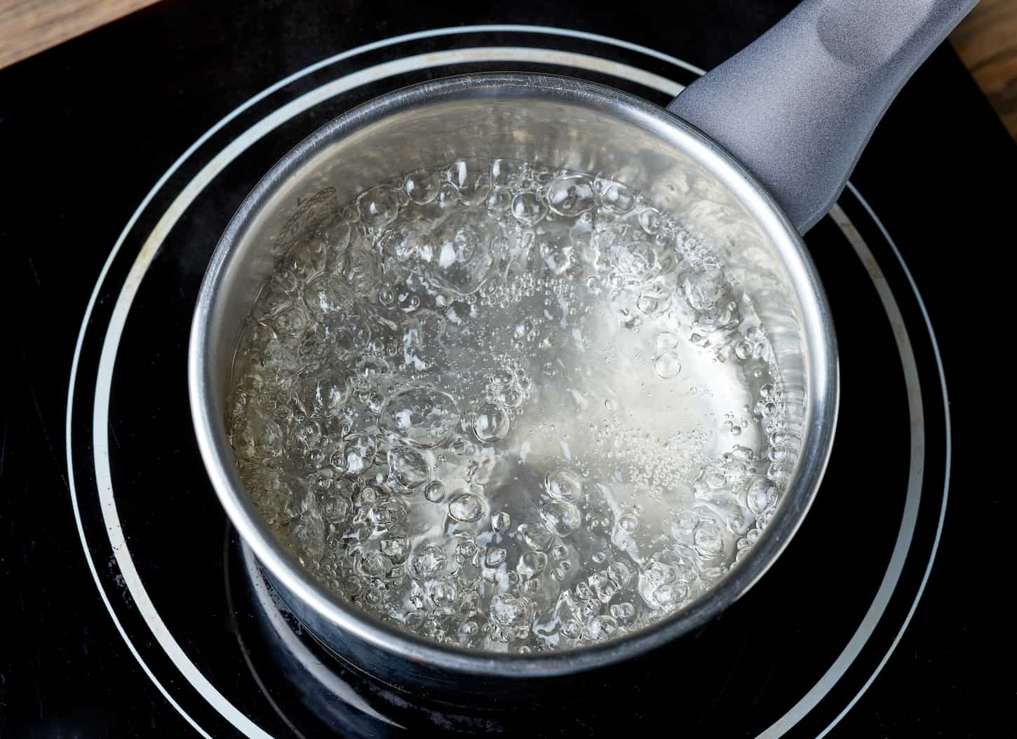 An image of kettle with boiling water on electric induction hob on wooden kitchen table.