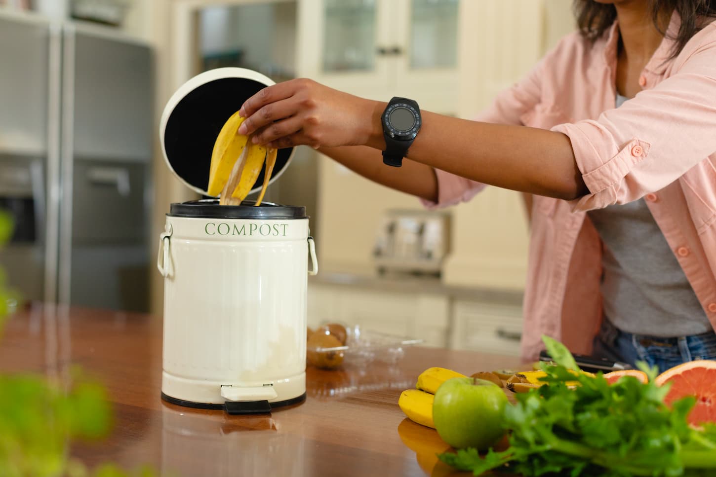 An image of a woman putting banana peel in a compost bin at home.