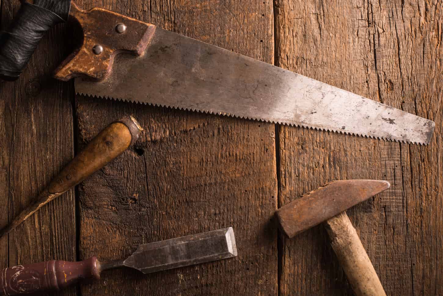 An image of an old rusty saw and other tools on top of a wood.