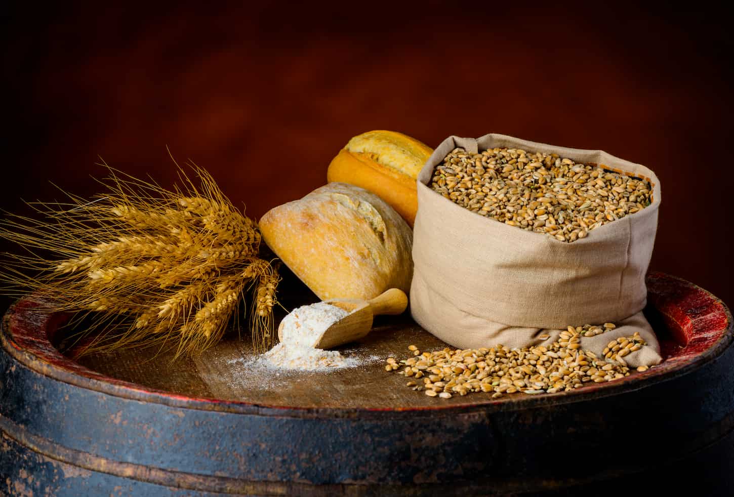 An image of Cereal products, wheat bun, cereal grain, and flour on a wooden barrel in a rustic setup.