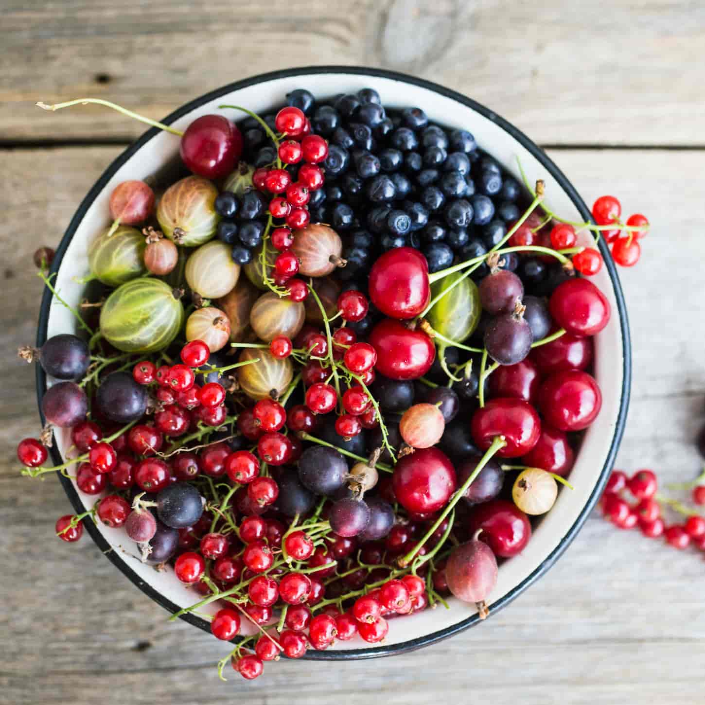 An image of different fresh berries in a white pot on the wooden background.