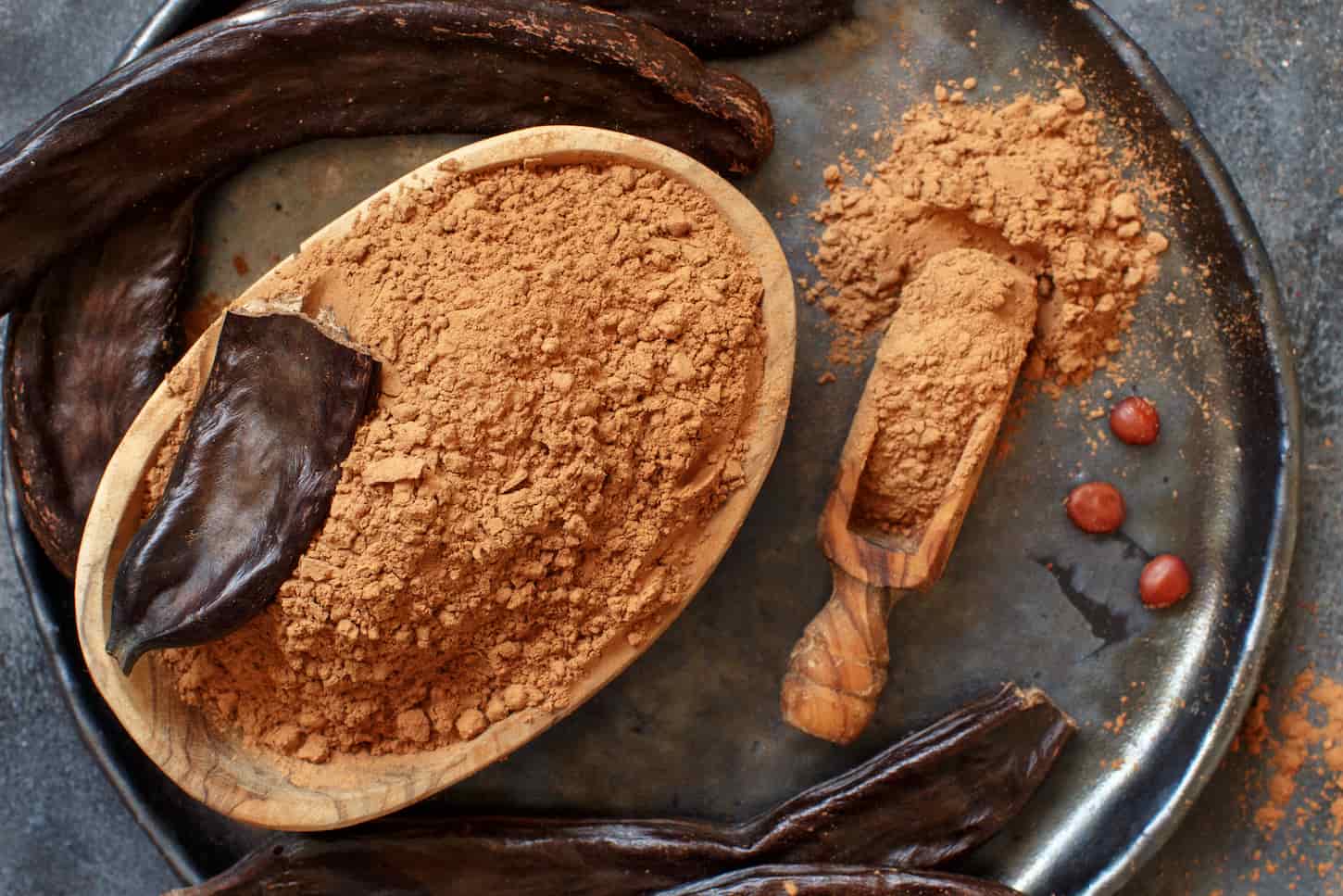 An image of a dry carob powder and pods top view on a grey table.