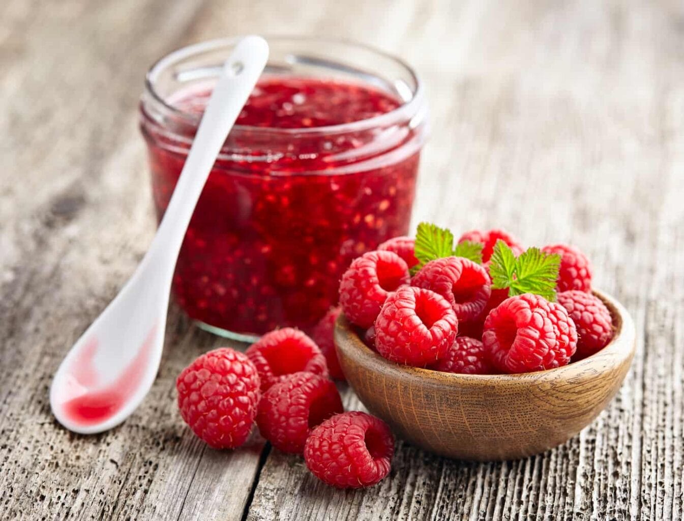 An image of a Raspberry jam with raspberry on a wooden board.