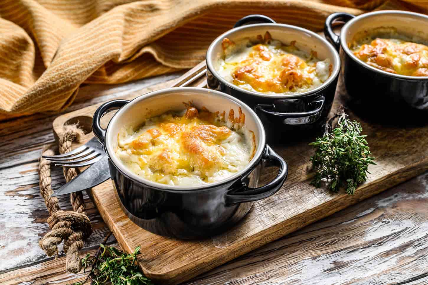 An image of Chicken and mushroom casserole in a clay pot on a wooden cutting board.