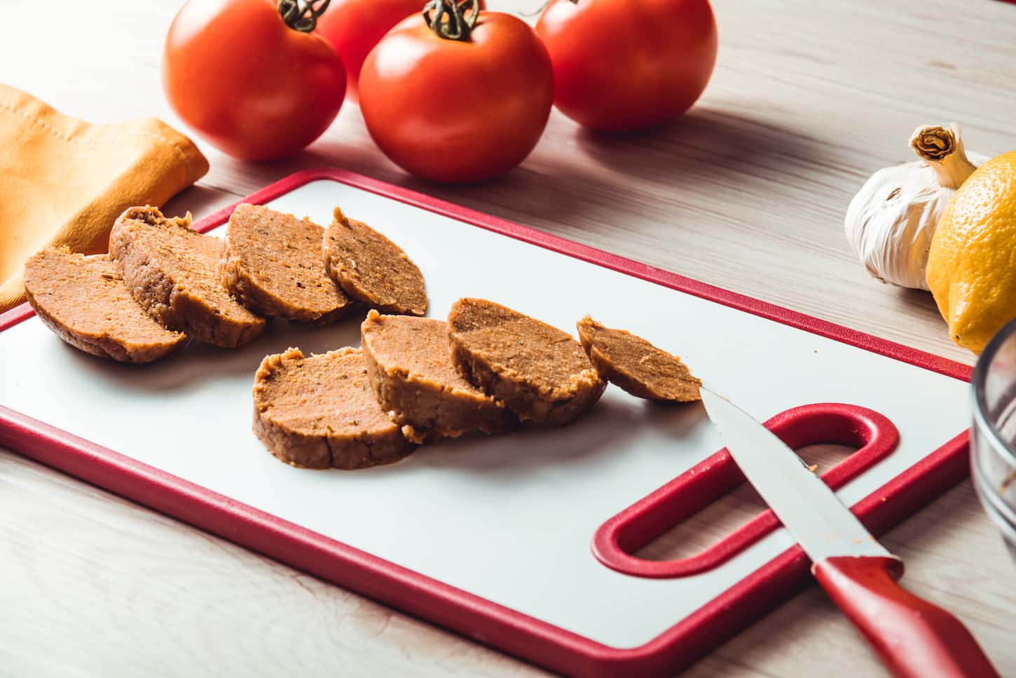 An image of a loaf and sliced seitan with tomatoes, garlic, and lemon in the background.