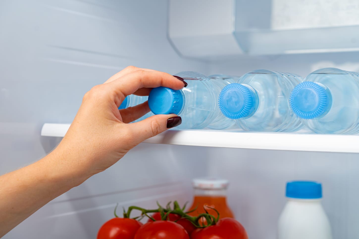 An image of a female hand taking bottle of water from a fridge.
