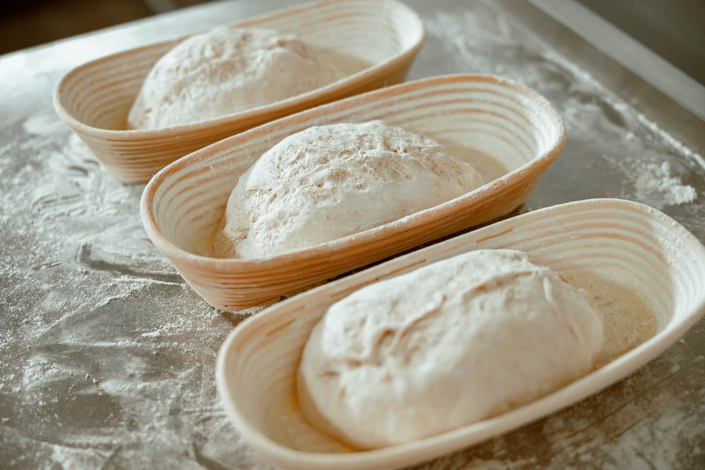 An image of Stylish ceramic dishes with raw bread loafs on metal table with scattered flour in modern bakery workshop.
