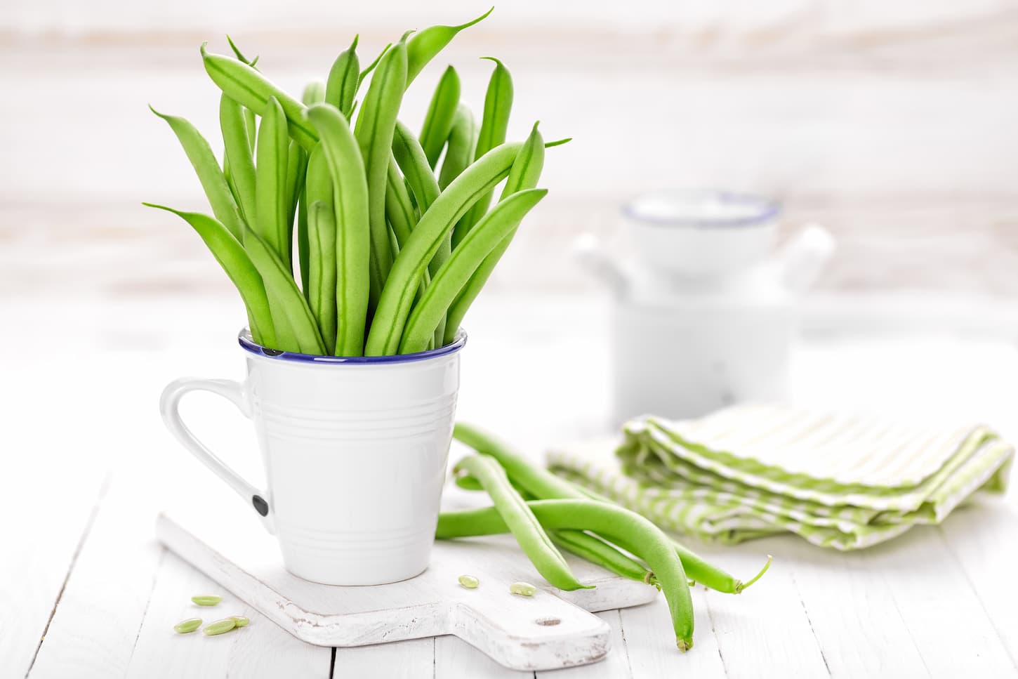 An image of green beans in a white mug on a white background.