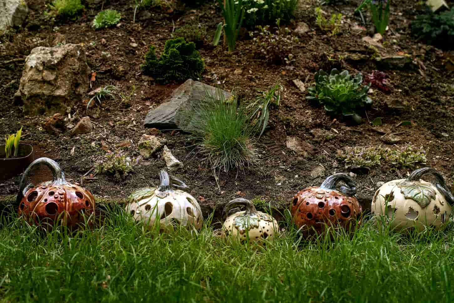An image of Halloween or Thanksgiving garden decorations, set of different hand crafted ceramic pumpkins standing in row on grass in wild garden. Fall holiday gardening.