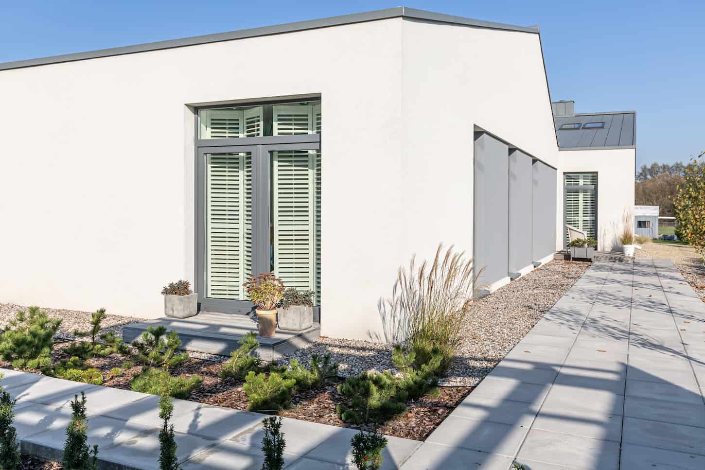 An image of a Residential House Backyard Garden with Concrete Stairs and a Grill Area Surrounded by Lawn and Flower Beds Decorated with Black Pebbles.