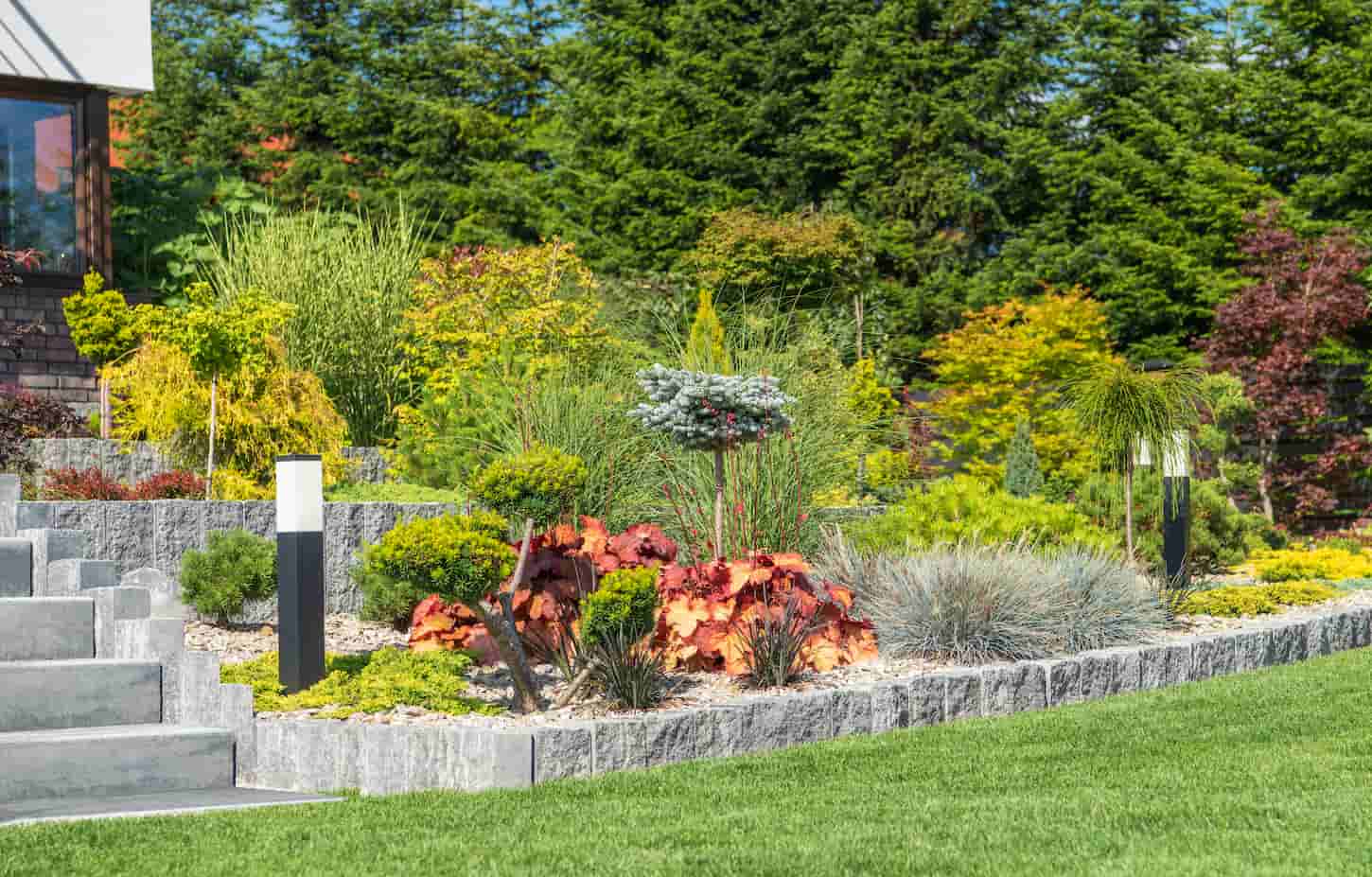 An image of a Beautiful Modern Rockery Garden in Front of a House. Concrete Garden Stairs and the Garden LED Lighting Next to Plants.