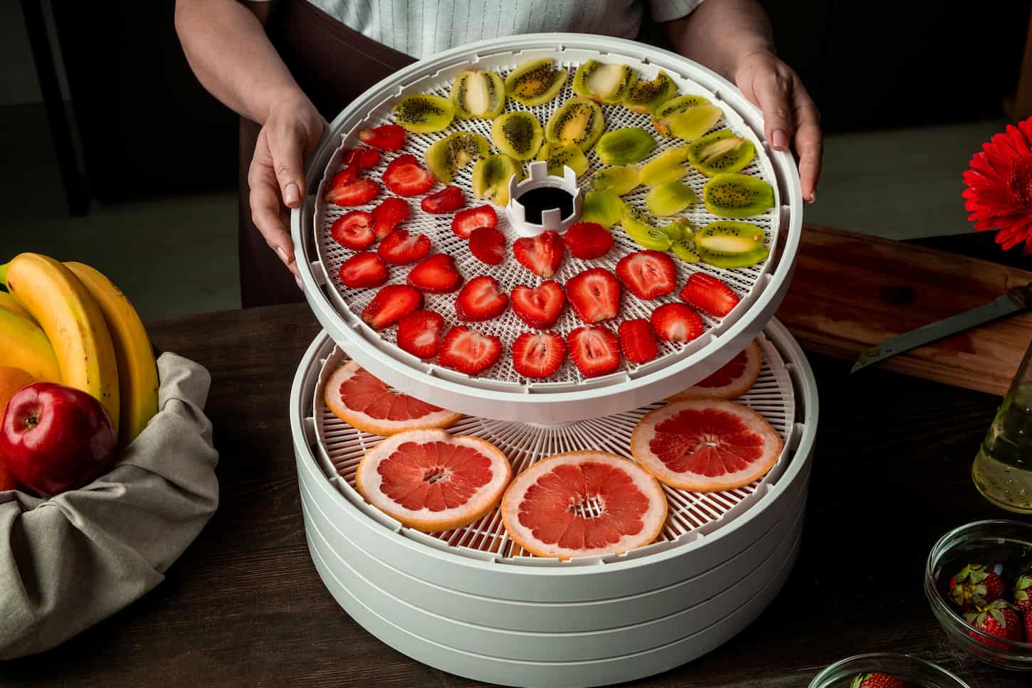 An image of an unrecognizable woman stacking dehydrator trays with sliced fruits while making organic snacks.
