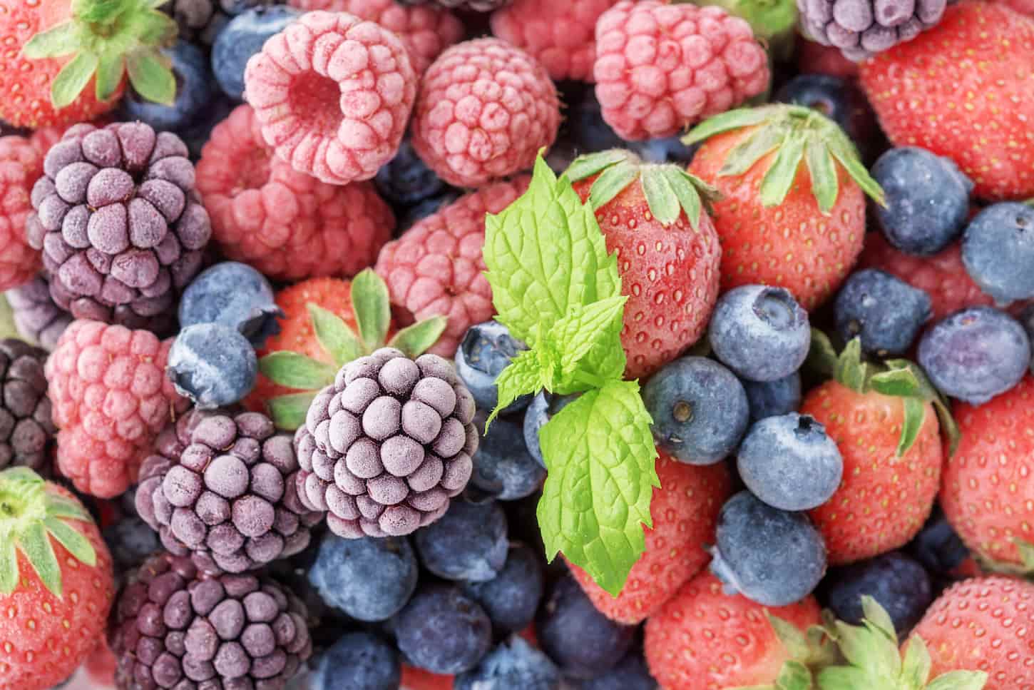 An image of frozen berries of raspberries, blackberries, and blueberries, covered with hoarfrost.
