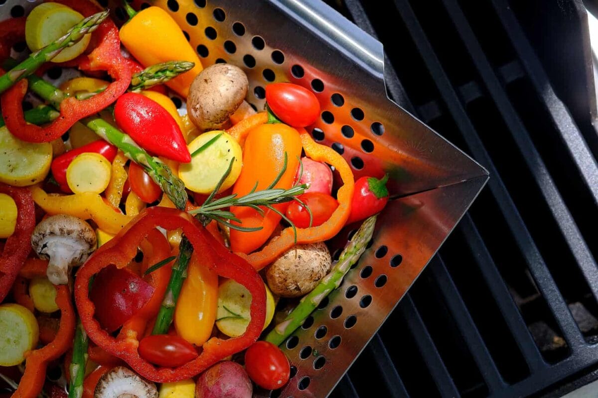 An image of a metal air-fryer basket with different vegetables.