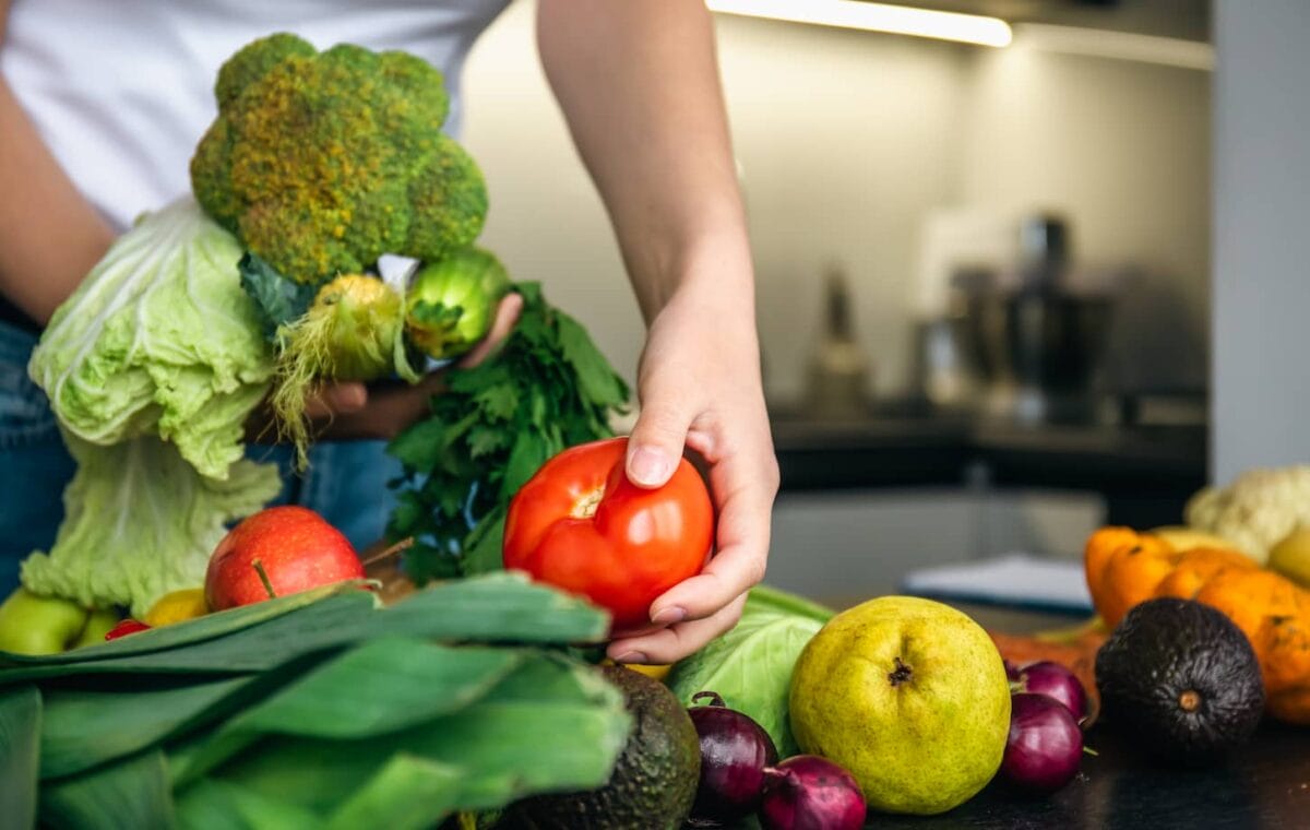 An image of a woman's hands sorting various fruits and vegetables on a kitchen counter for food preparation.
